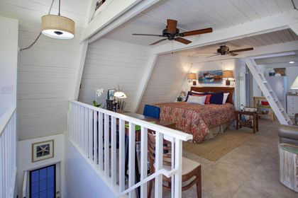 Stairs lead to the main living area with queen bed, wiring desk, leather sofa, streaming TV, and plenty of natural light.