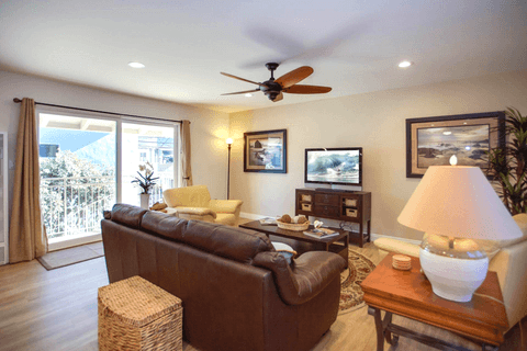Sliding glass doors open into the main living area of the apartment, which includes leather sofa and side chairs, cable TV, and an open floor plan concept.