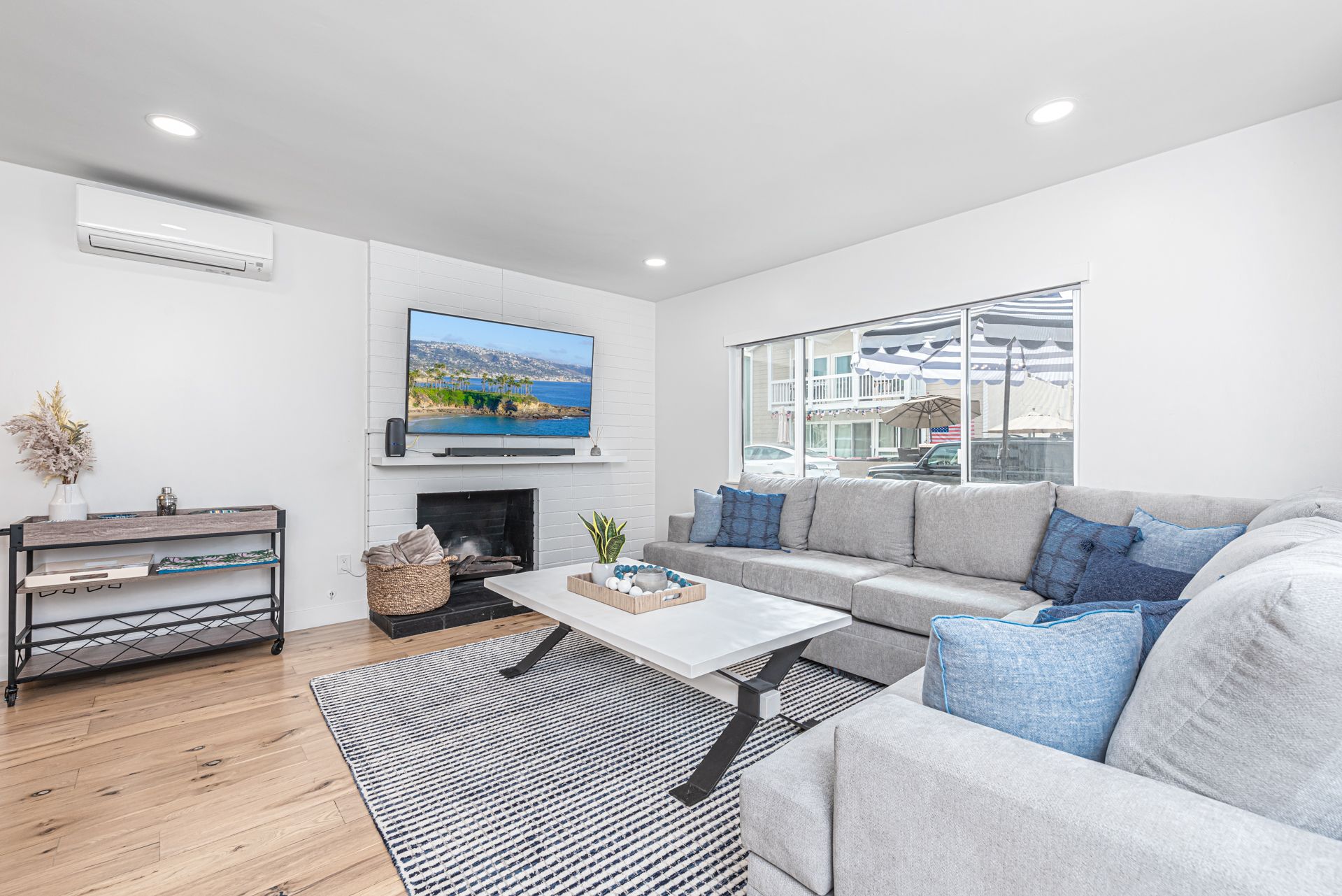 The main living area includes a large L-shaped sofa, TV, and wall unit A/C.