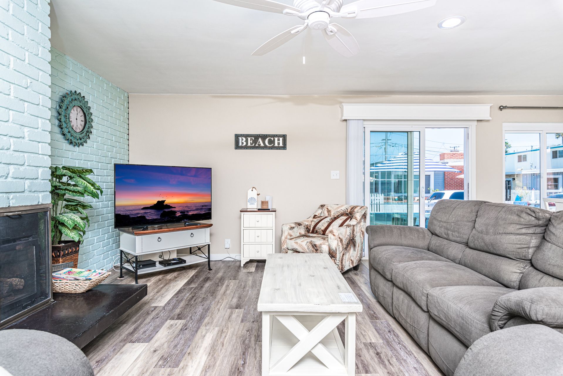 The living room includes a sofa, two upholstered side chairs, TV, and sliding glass doors out to the front patio. Perfect for unwinding after a day at the beach.